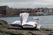 An open book and empty tea cup sitting by the seaside, pages billowing in the breeze.